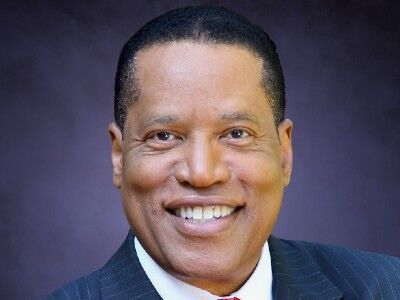 Smiling man in a dark pinstripe suit against a purple studio background