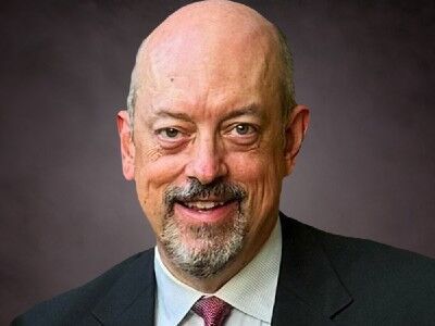 Smiling bald man in a dark suit and tie against a gray studio background