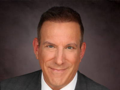 Headshot of a smiling man in a dark suit against a gray studio background