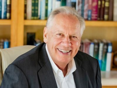 Smiling man in a dark suit seated before bookshelves in a library