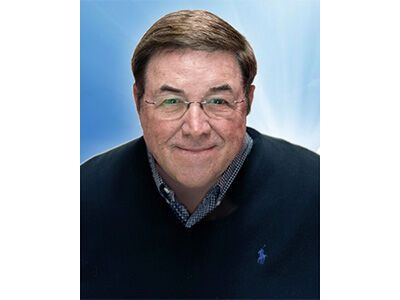 Smiling man in glasses and navy sweater against a light blue background