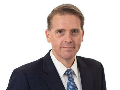 Portrait of a man in a dark suit and blue tie against a white background