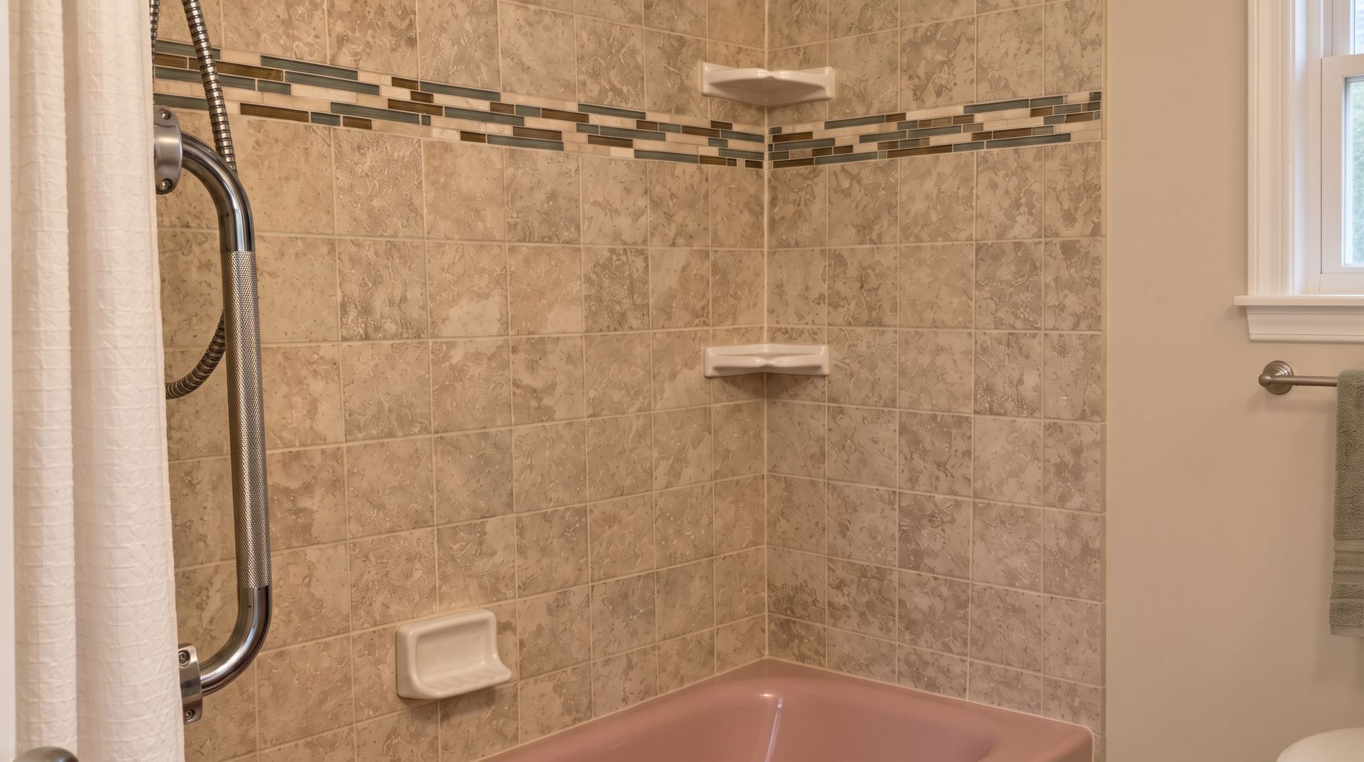 Bathroom shower with beige tile, built-in shelves, grab bar, and a pink tub edge