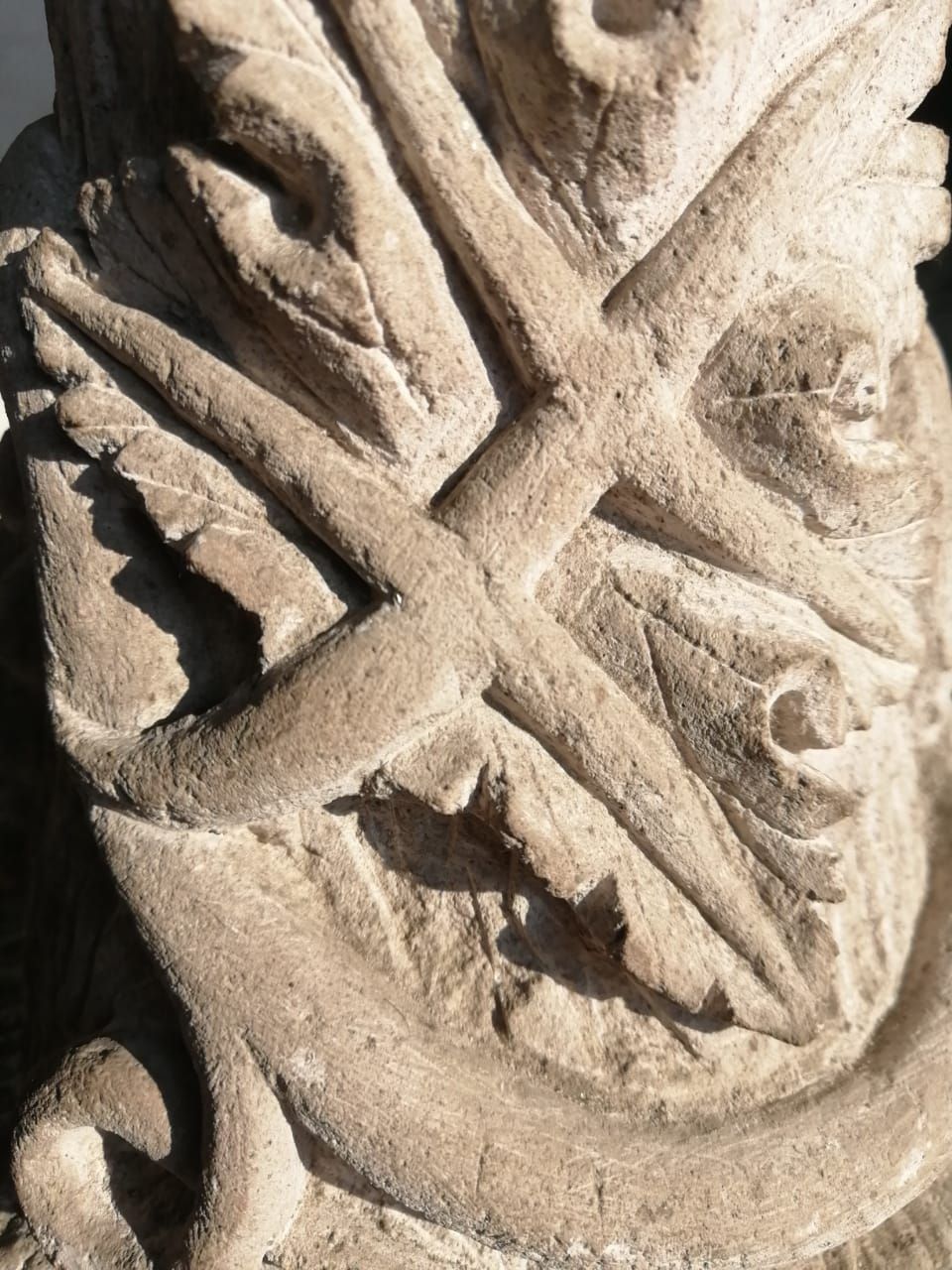 Primer plano de una talla de piedra beige desgastada por el tiempo, con motivos de hojas entrelazadas y diseños decorativos en espiral.