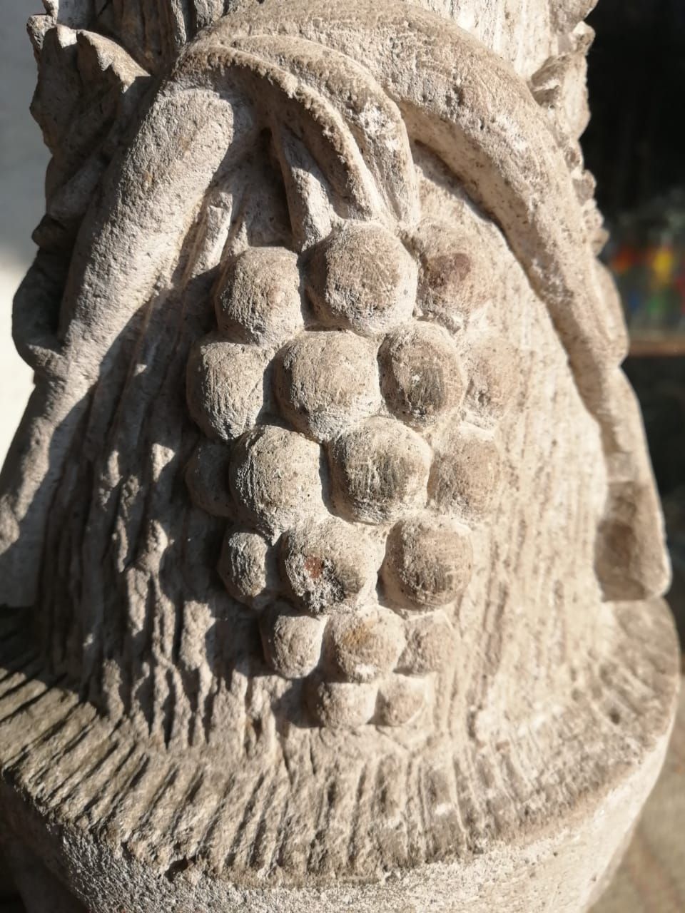 Una escultura de piedra que representa un racimo de uvas y espigas de trigo estilizadas, rematada con una base decorativa.