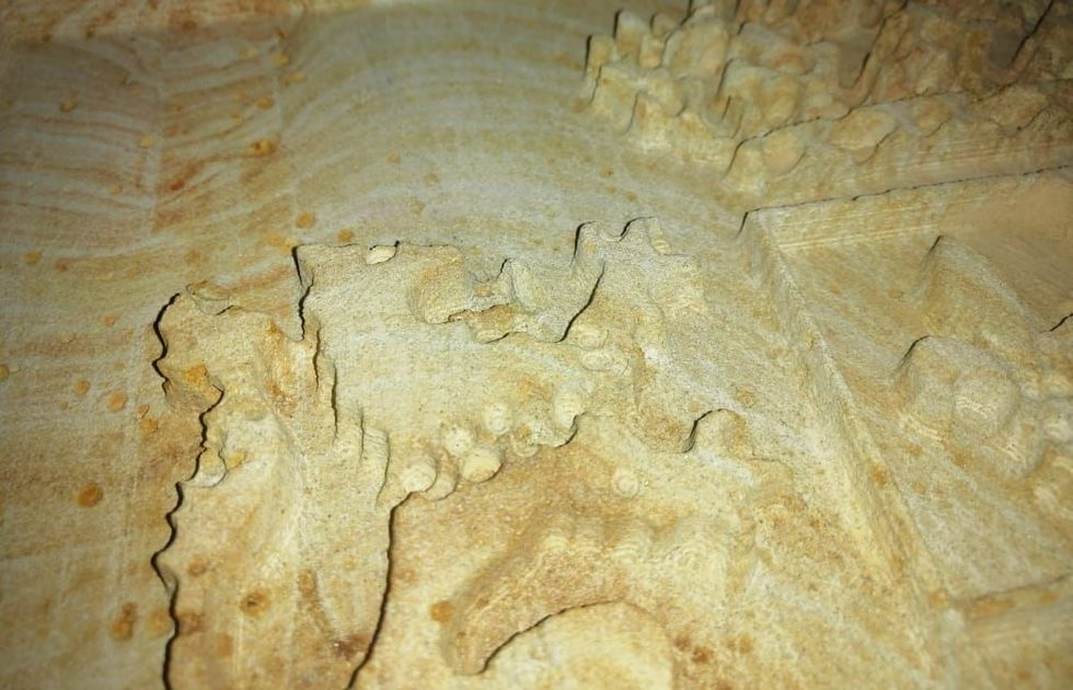 Primer plano de una superficie de piedra tallada de color marrón claro con relieves y bordes texturizados e irregulares.