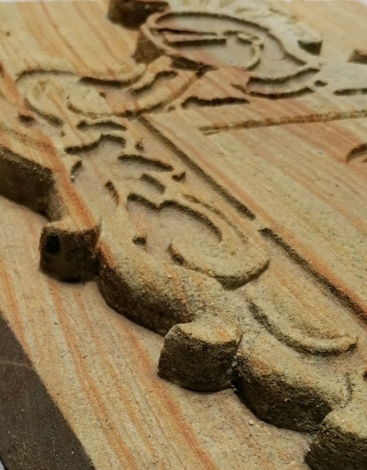 Primer plano en ángulo de un relieve decorativo tallado en madera clara, con motivos ornamentales y un emblema circular.