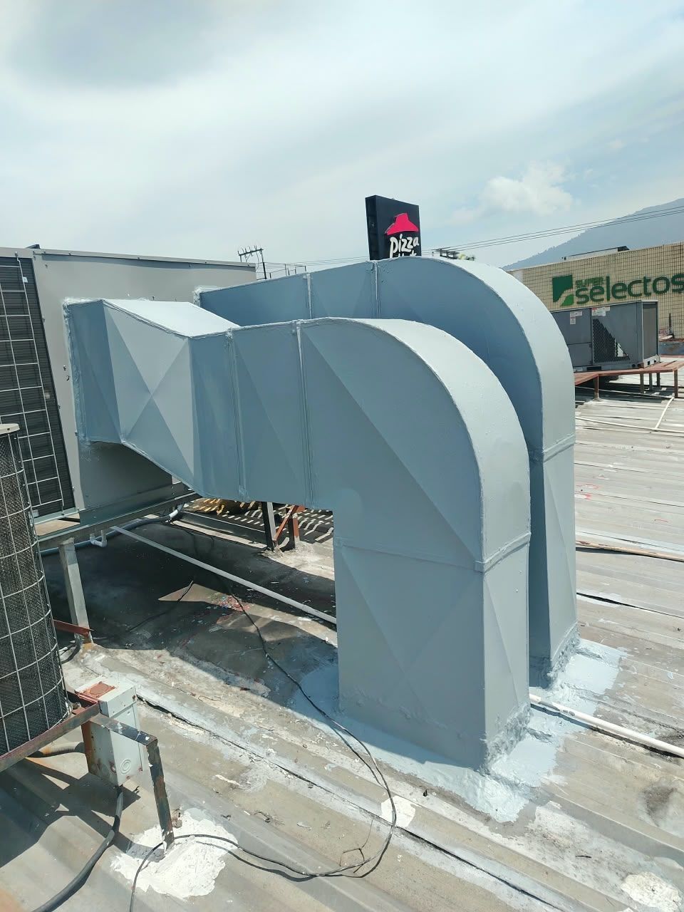Gran conducto blanco de ventilación y equipos de climatización en la azotea de un edificio comercial bajo un cielo brillante.
