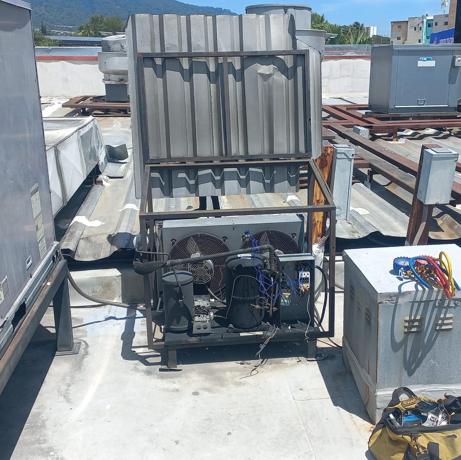 Unidad de climatización en la azotea con conductos y maquinaria, expuesta a la luz solar directa, rodeada de equipos eléctricos y escombros.