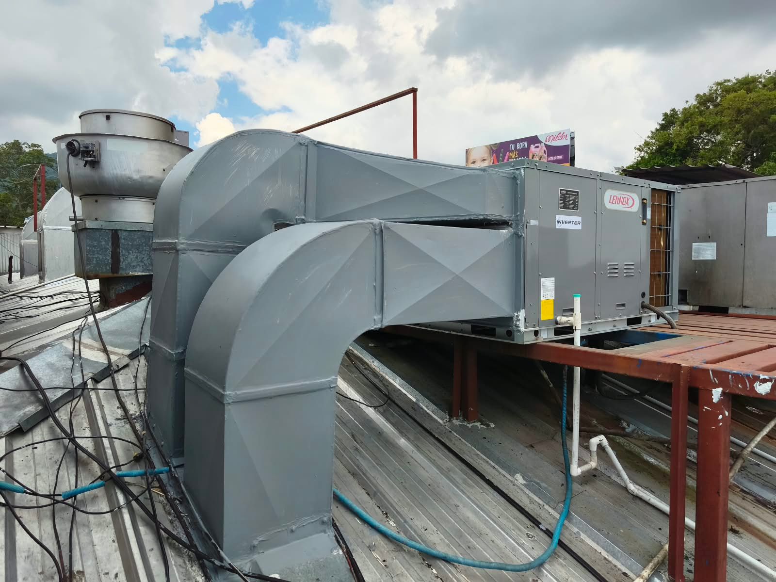 Grandes conductos grises de climatización y equipos de ventilación en la azotea de un tejado industrial plano.