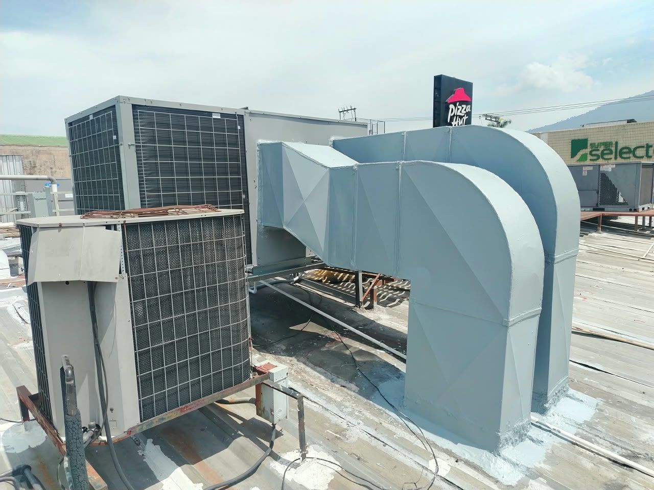 Unidades de climatización en la azotea con grandes conductos plateados en el tejado de un edificio comercial.