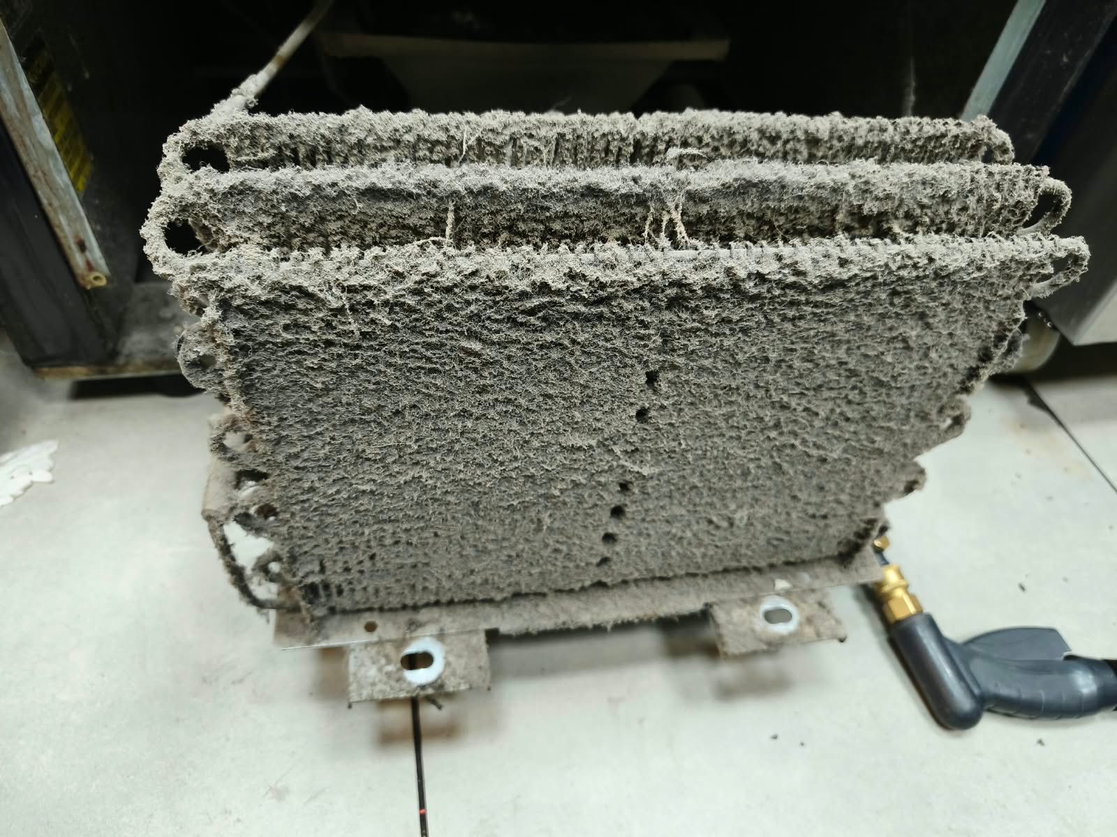Radiador o intercambiador de calor metálico cubierto de polvo con tuberías en el suelo de un taller.