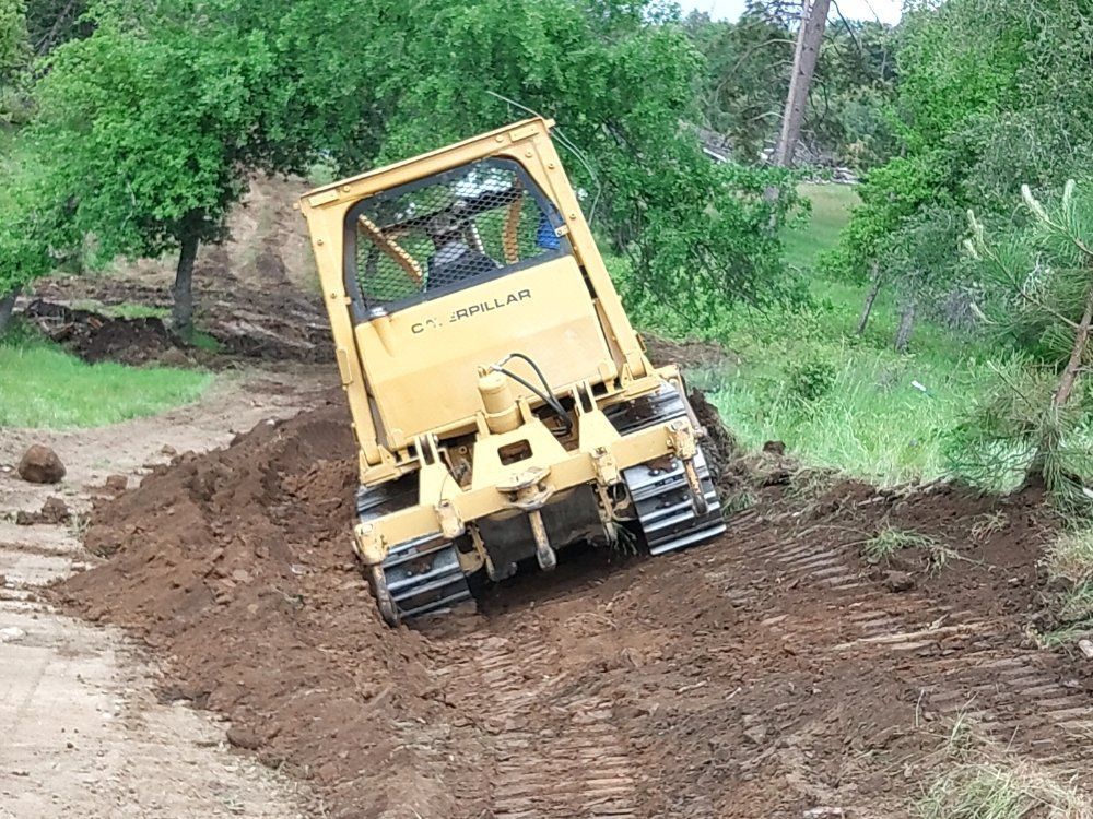 Yellow tracked vehicle driving through muddy dirt path in a green wooded area