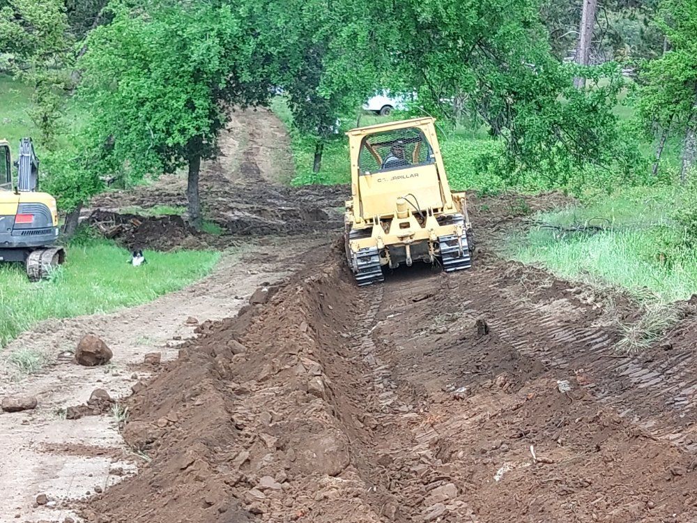 Yellow bulldozer grading a muddy dirt road in a green wooded area