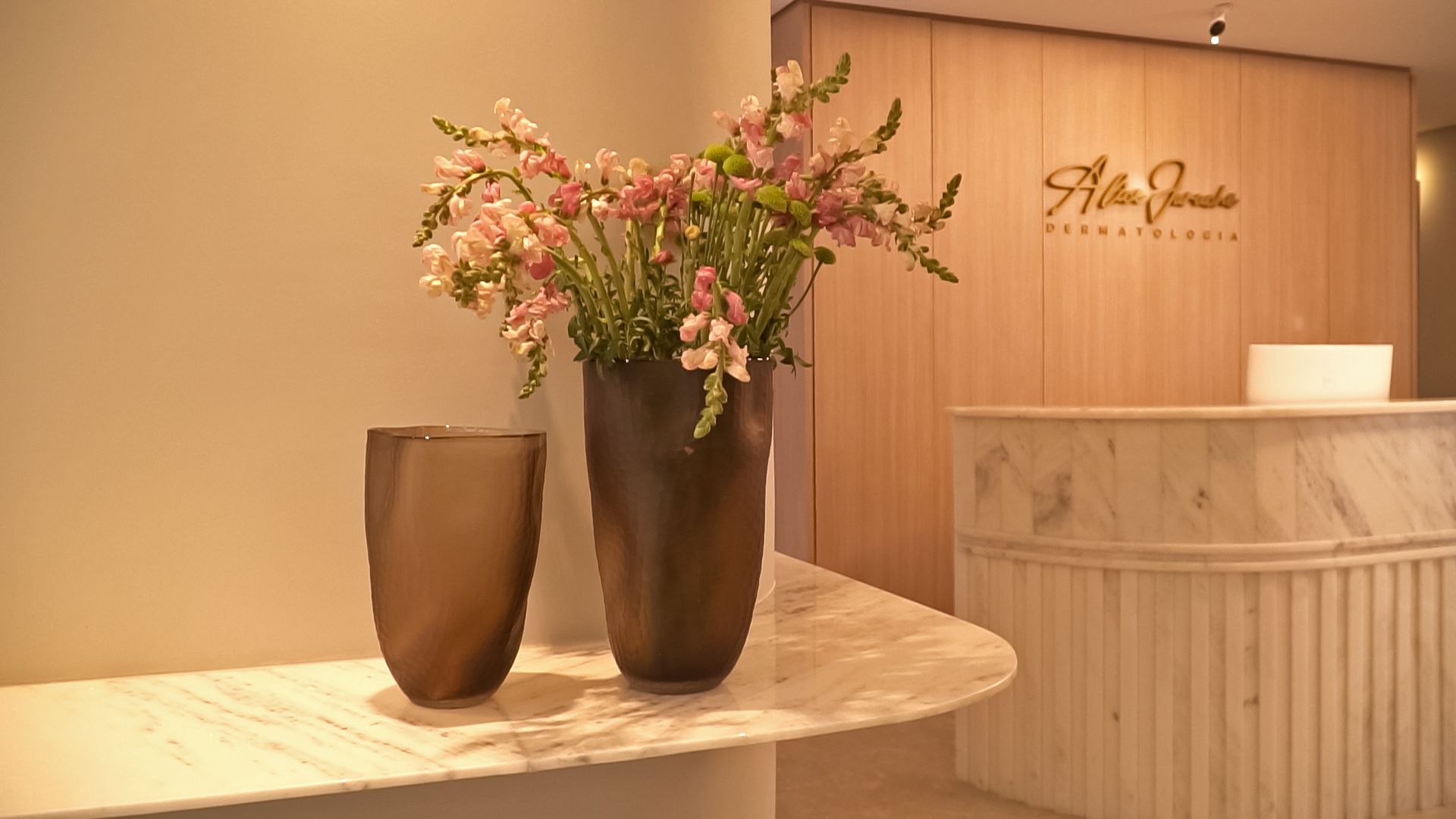 Dois vasos de flores estão sobre uma mesa em frente a uma recepção.