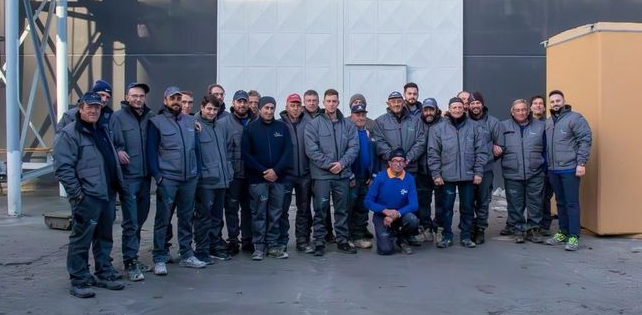 Un gruppo di uomini in abiti da lavoro sono in piedi fuori da un edificio e posano per una foto.