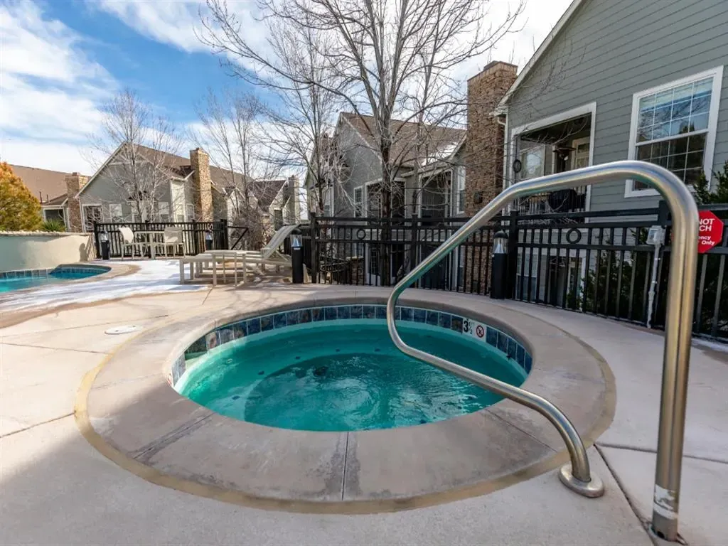 Outdoor hot tub and swimming pool area with lounge chairs and tables.