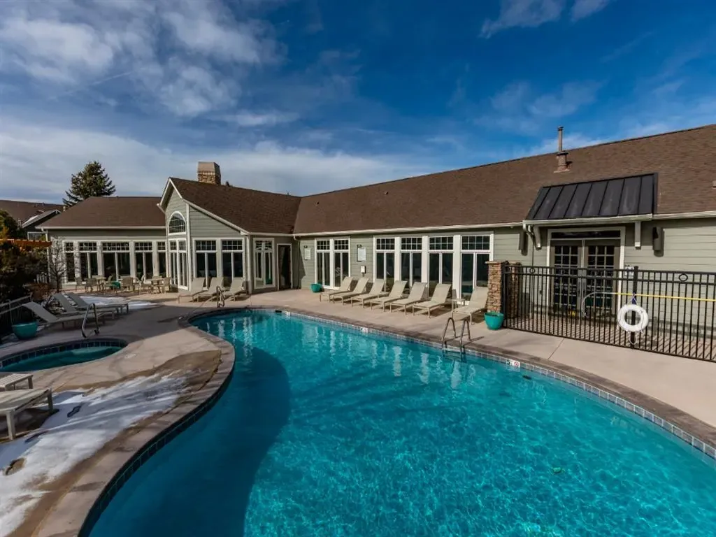 Outdoor swimming pool and hot tub with lounge chairs and building in background.