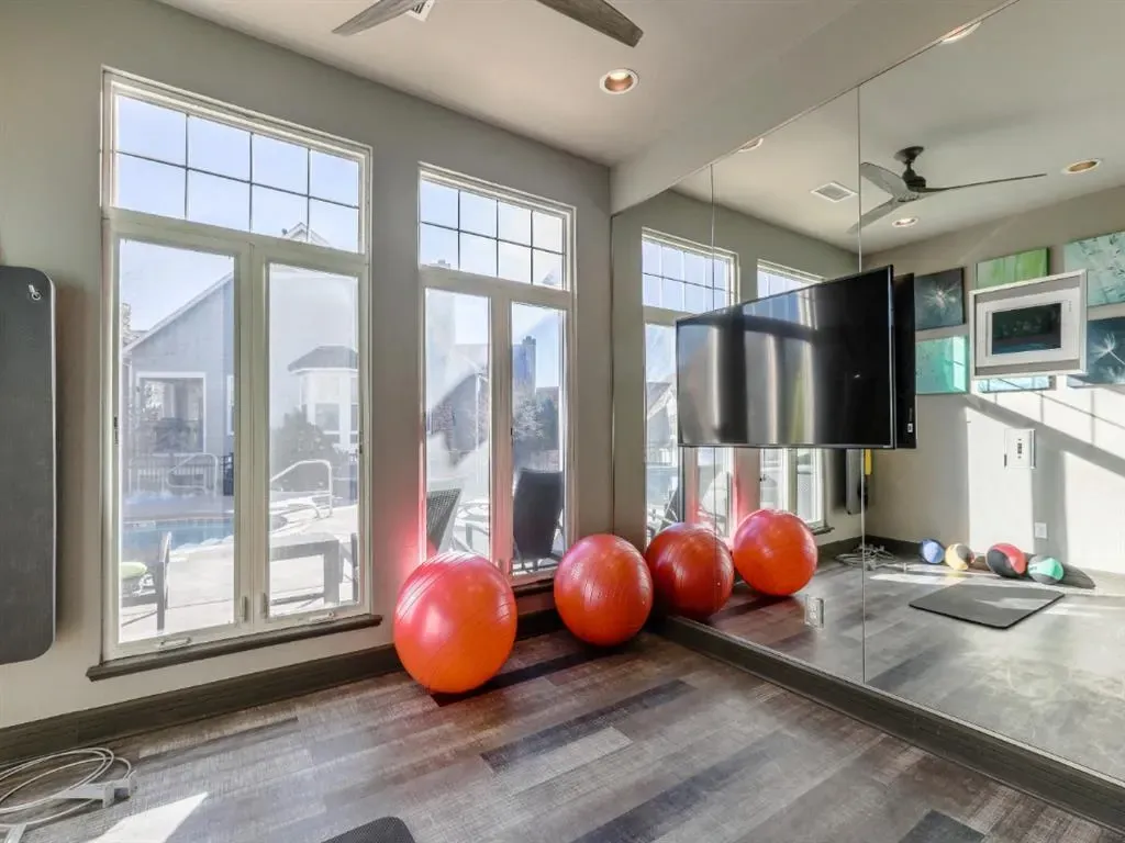 Gym room with exercise balls, TV, and mirrors, overlooking a pool area.