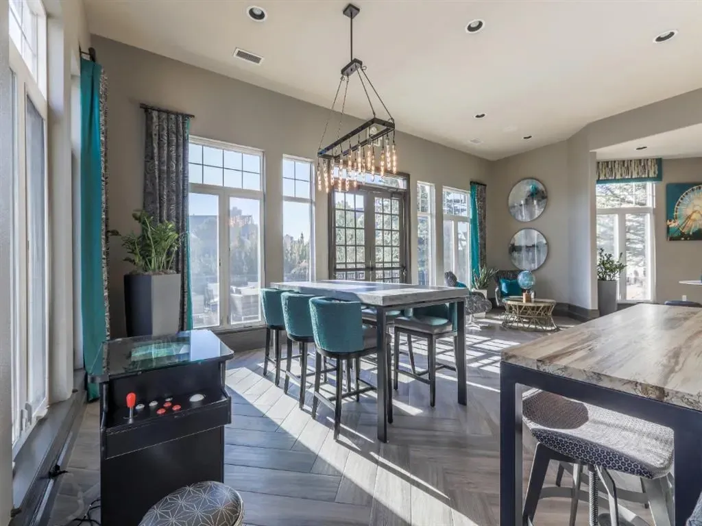 Community lounge with arcade game, dining table, bar stools, and seating area with large windows.
