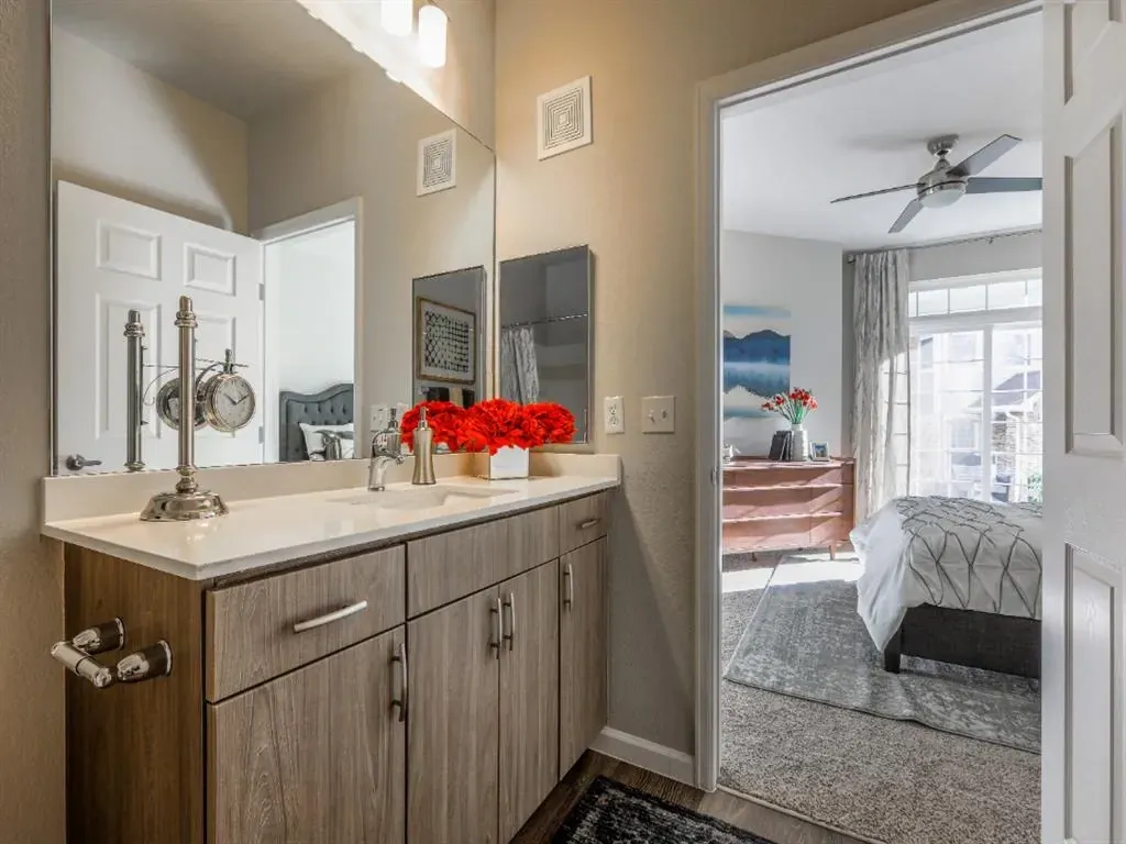 Modern bathroom vanity with double sink and large mirror, looking into a bedroom.