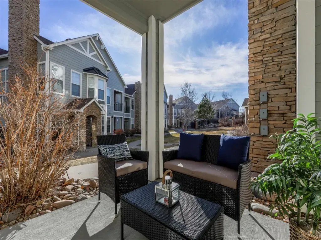 Covered porch with seating area overlooking apartment buildings.