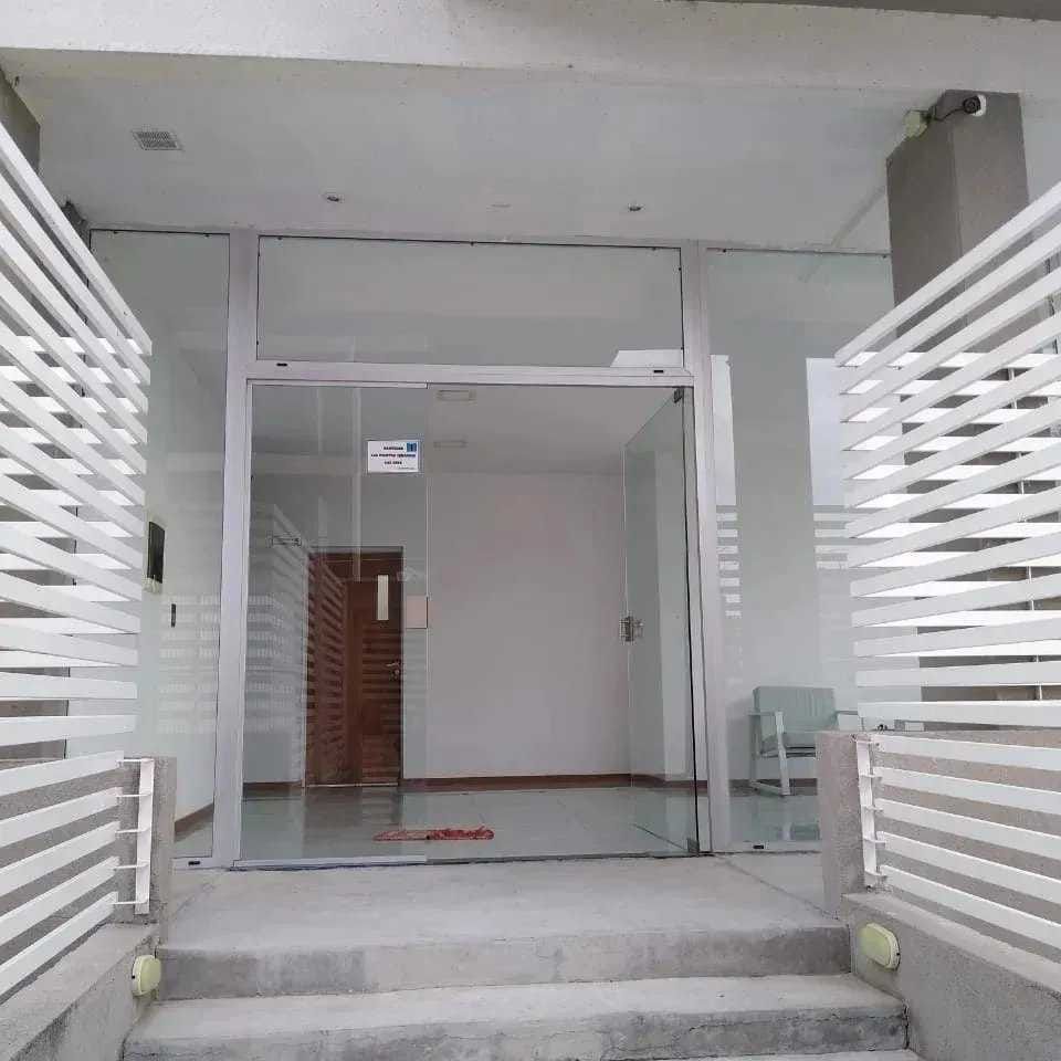 Entrada moderna al edificio con escalones, puertas de cristal y paredes laterales con listones blancos.