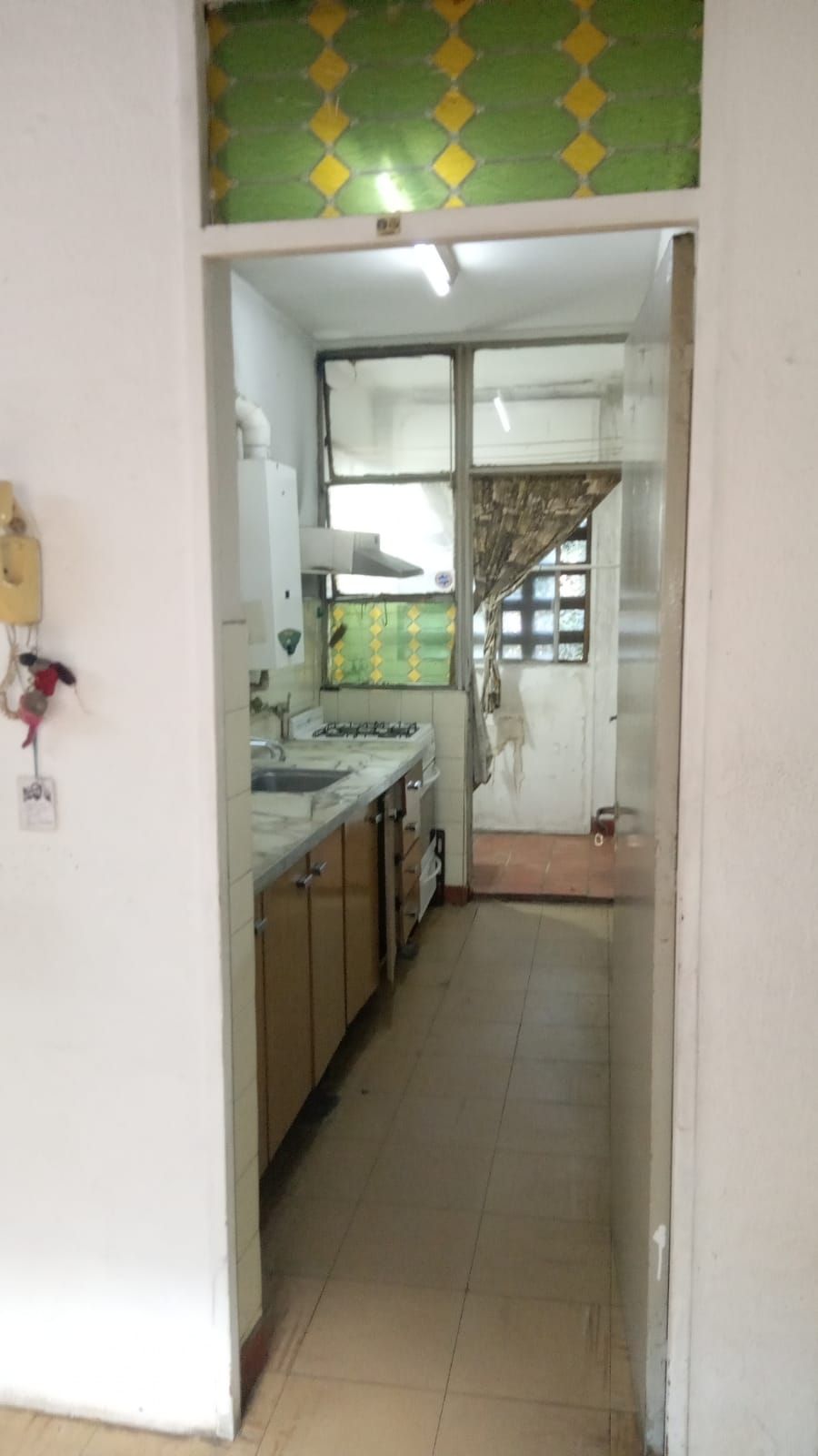 Habitación blanca vacía con suelo de baldosas, puerta y una pequeña ventana cerca del techo.