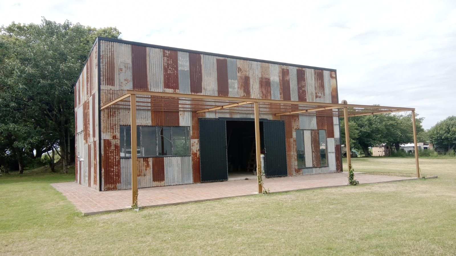 Pequeño edificio beige con un tanque de agua en un campo de hierba bajo un cielo nublado.