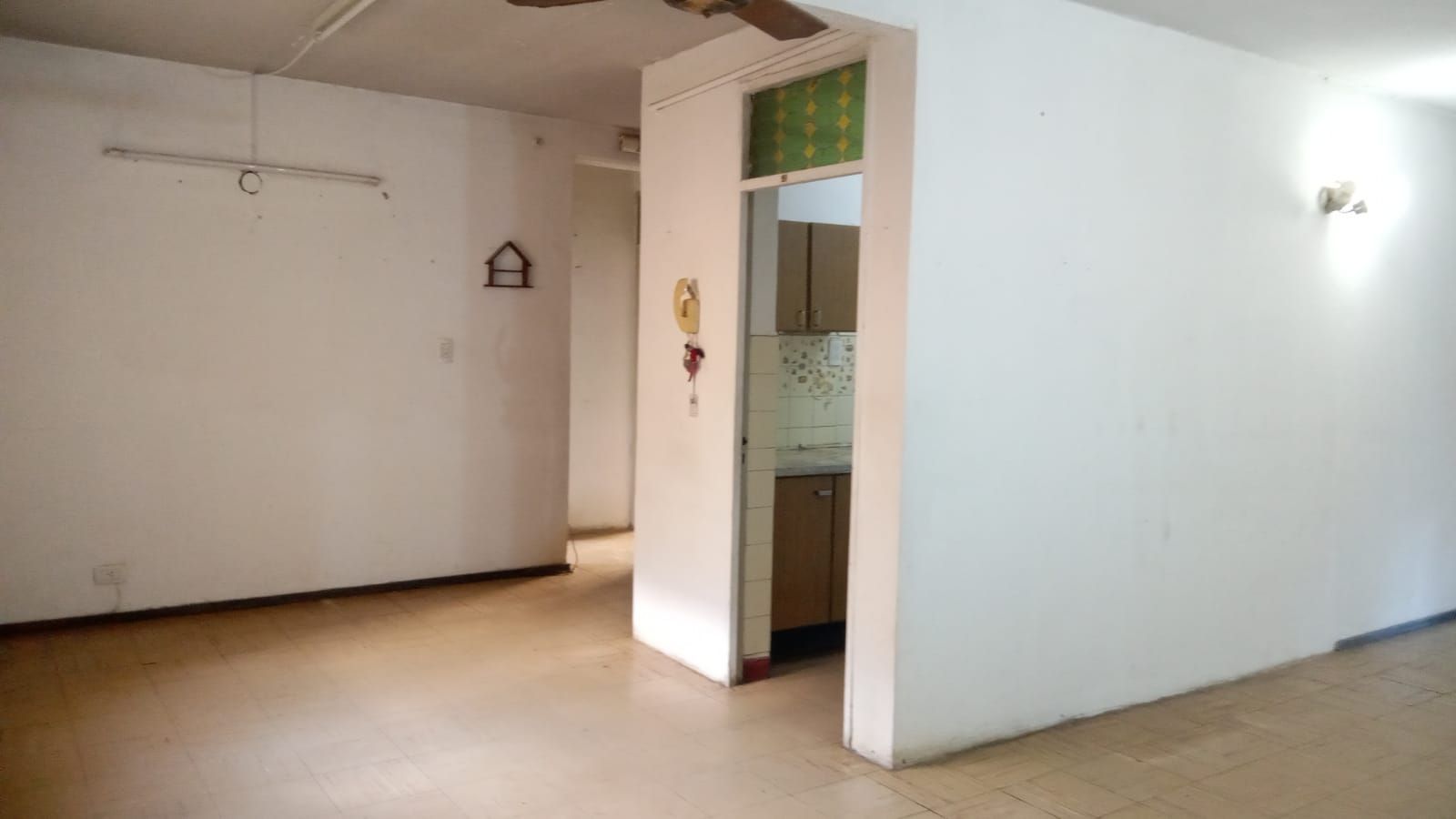 Habitación blanca vacía con suelo de baldosas, puerta y una pequeña ventana cerca del techo.