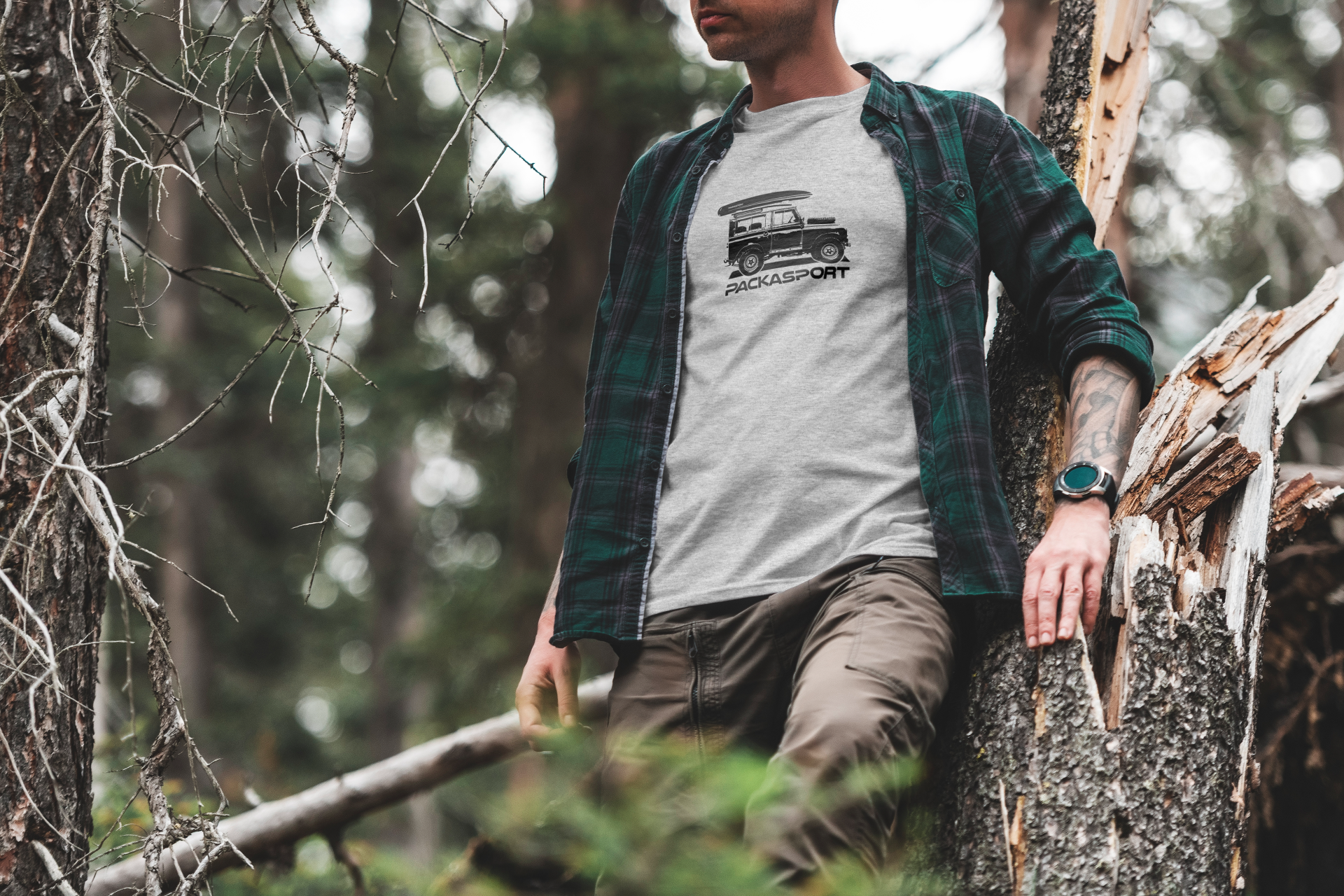 A man in a plaid shirt is standing next to a tree in the woods.