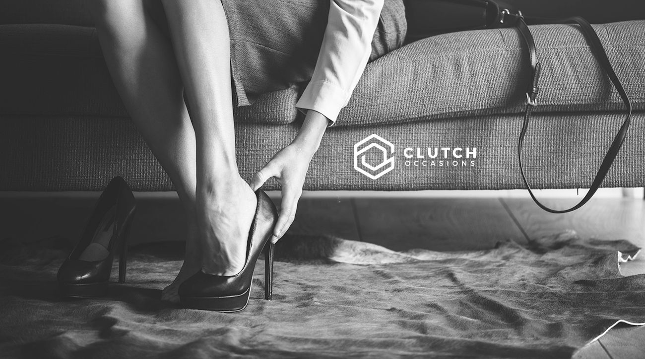 A woman is putting on her high heels while sitting on a couch.