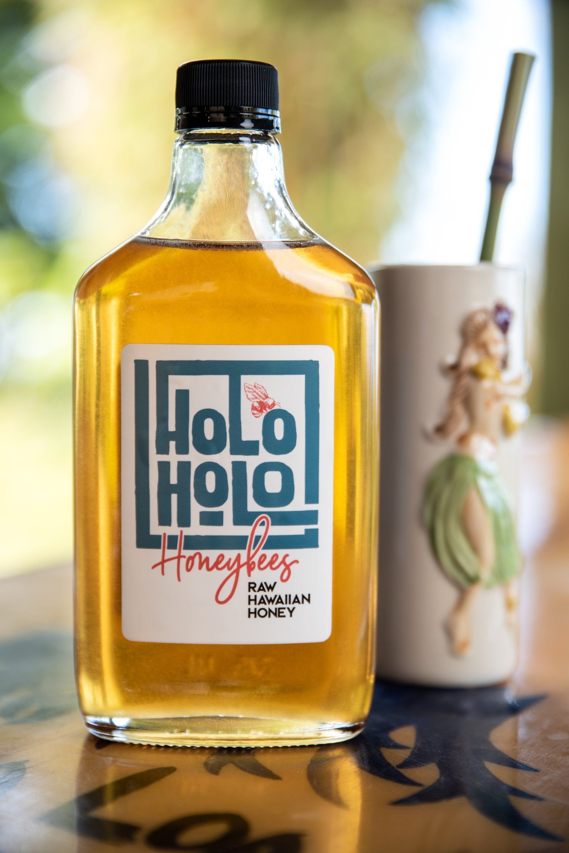A bottle of honey next to a cup with a hula girl on it.