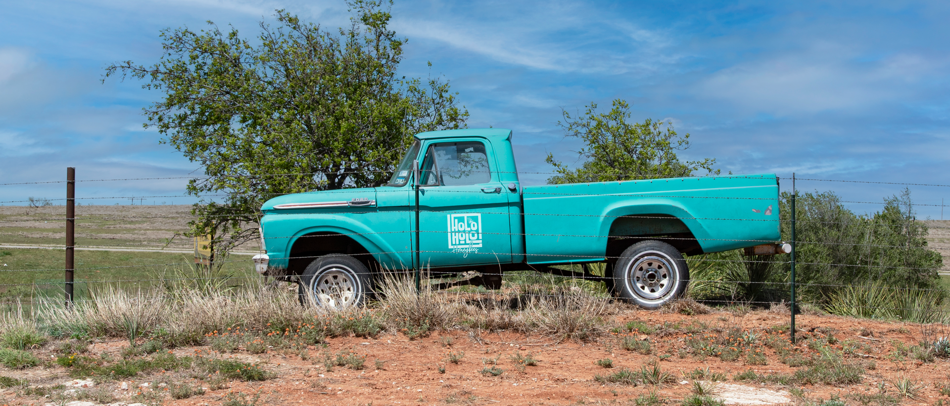 A blue truck is parked in the middle of a dirt field.