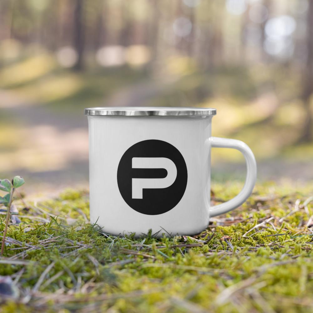 A white mug with a black letter p on it is sitting in the grass.