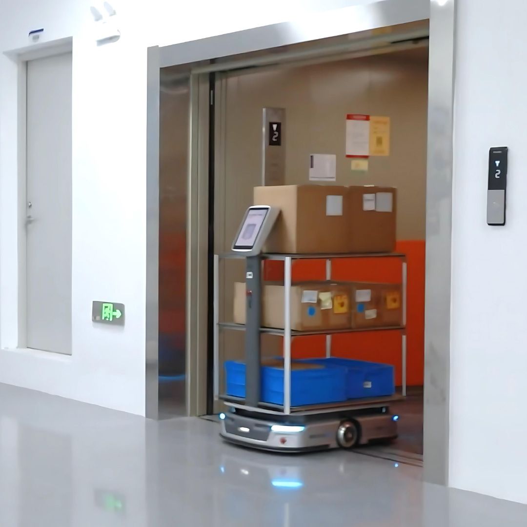 Robot carrying packages in an elevator. The robot is silver and blue with boxes on its shelves. Bright interior.