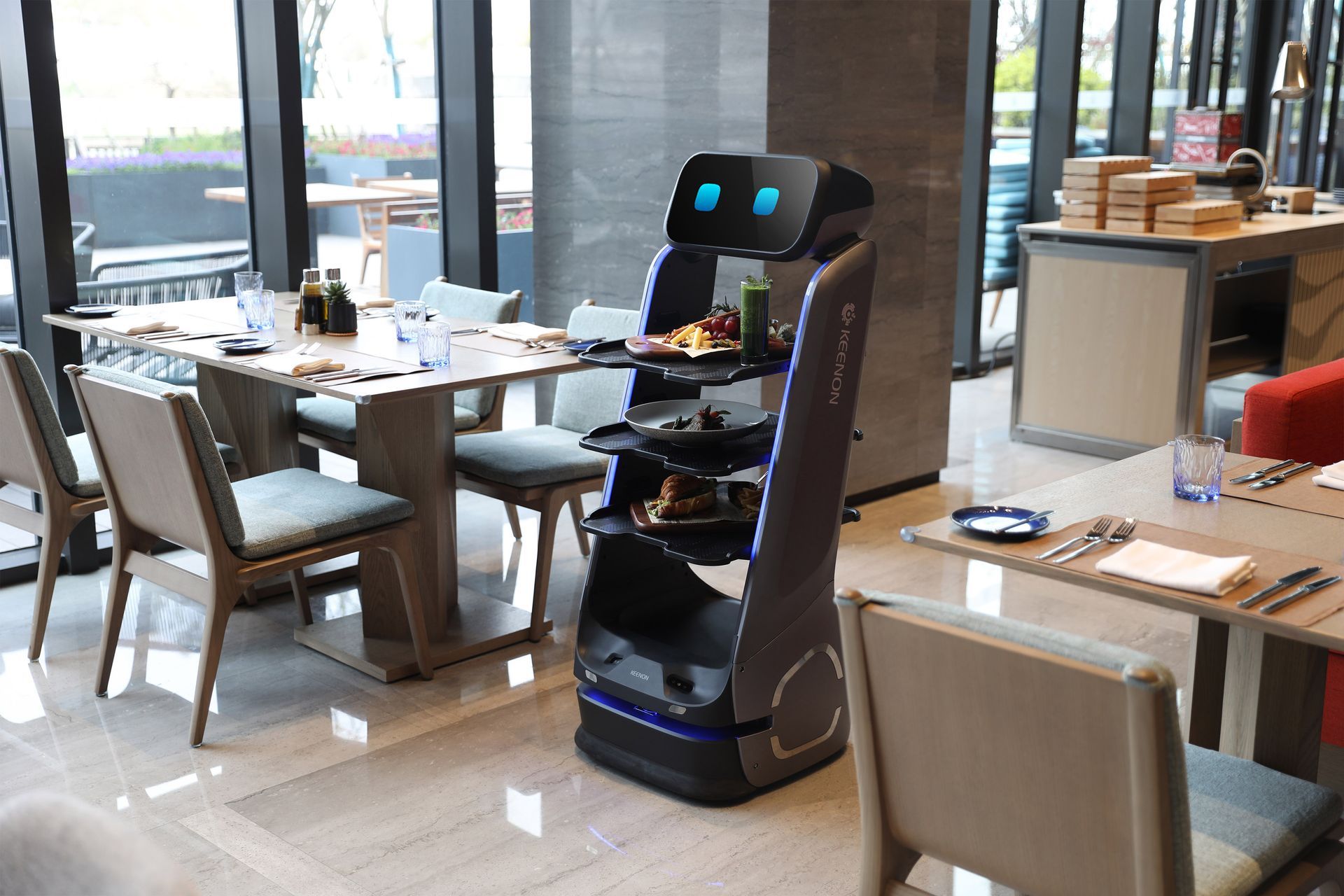 A food service robot with trays holding food and drinks. It is inside a restaurant.
