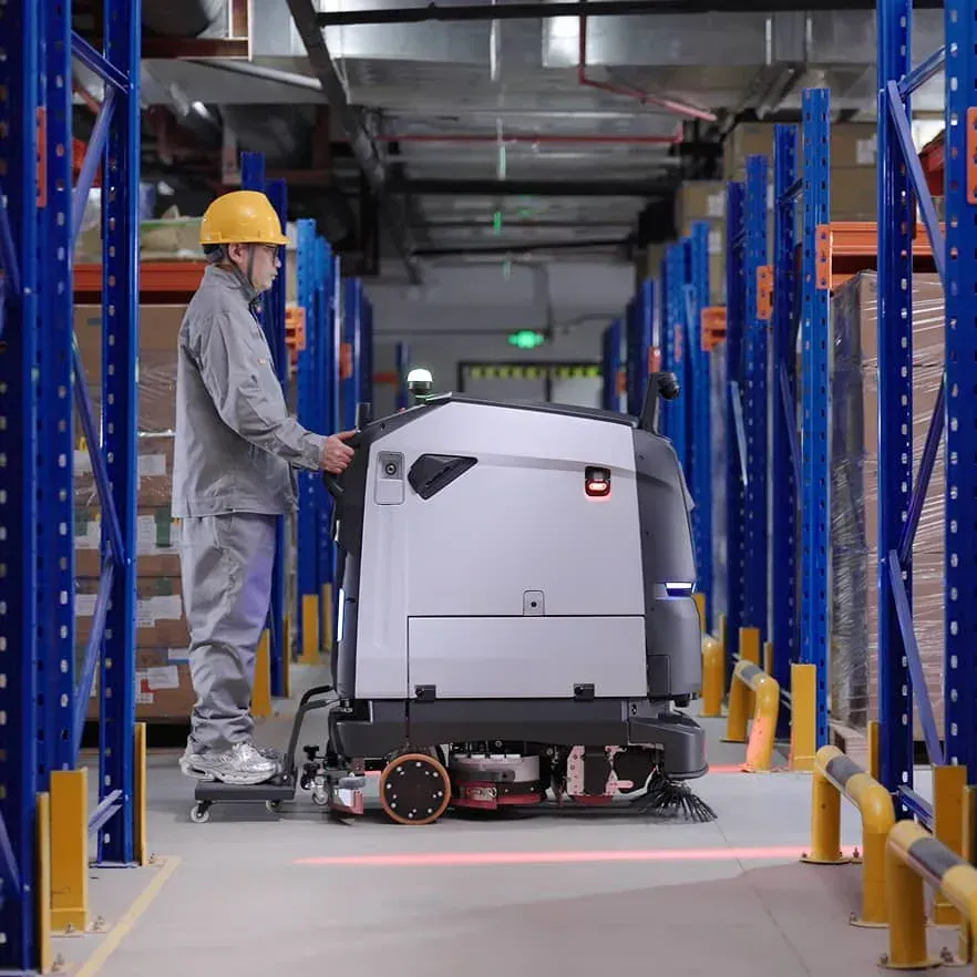 Worker in a warehouse operating a white automated cart between tall blue storage racks.