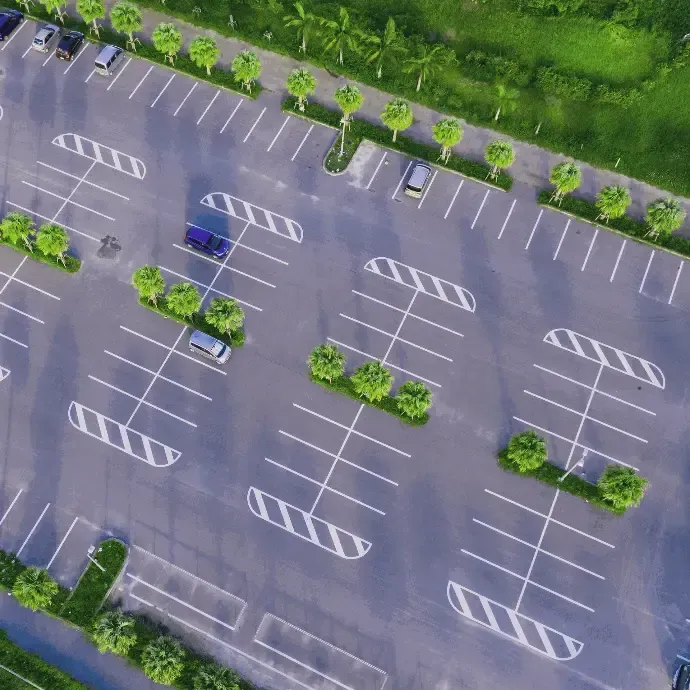 Aerial view of an empty parking lot with white-lined spaces and scattered trees nearby
