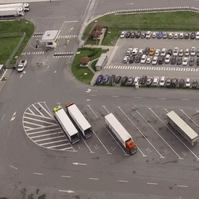Aerial view of a parking lot with several semi-trucks, cars, and an empty intersection.
