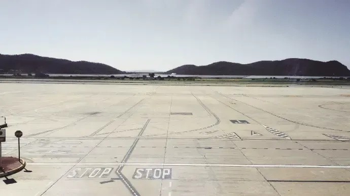 Wide airport tarmac with STOP marking, distant hills, and clear sky