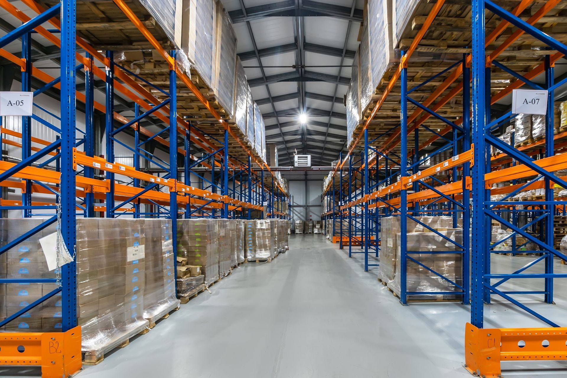 Wide warehouse aisle with tall blue-and-orange racks and stacked pallets