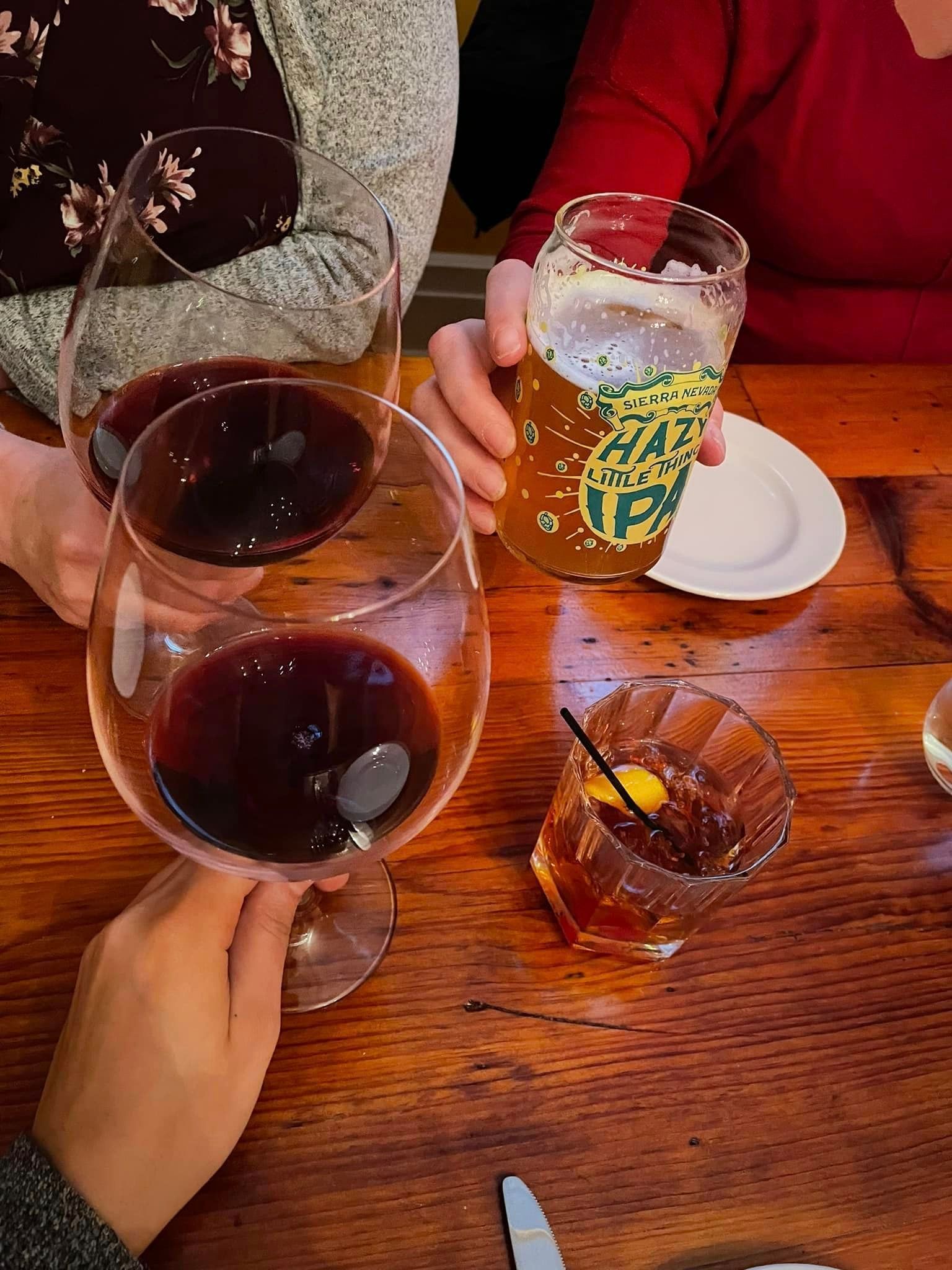 A group of people are sitting at a table holding glasses of wine and beer.