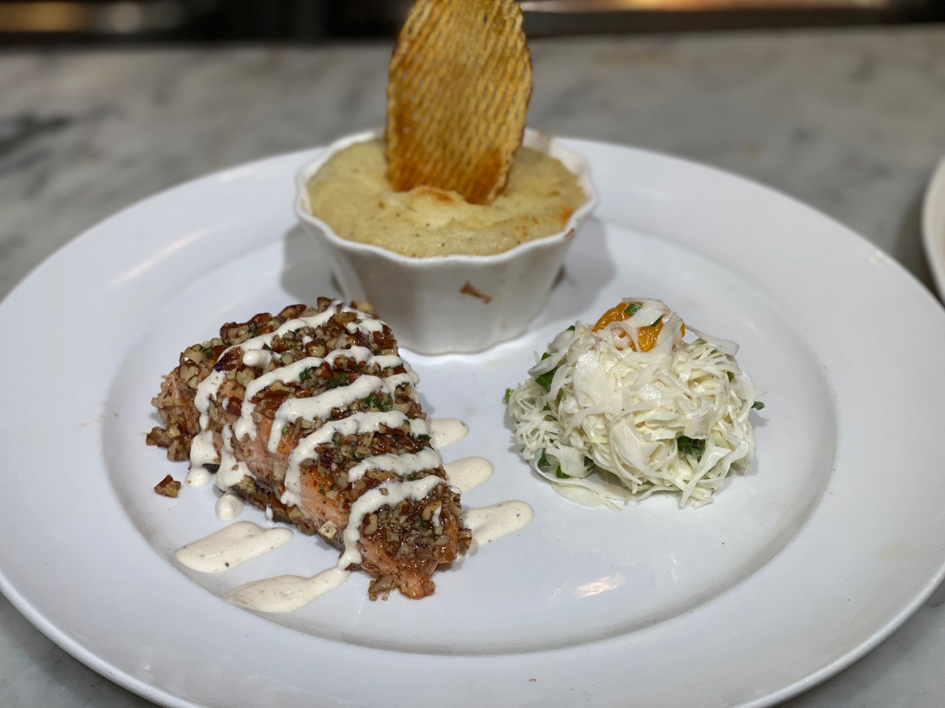 A white plate topped with a piece of meat , coleslaw and mashed potatoes.