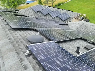 Rooftop covered with solar panels and skylights, with trees and grass visible in the background.