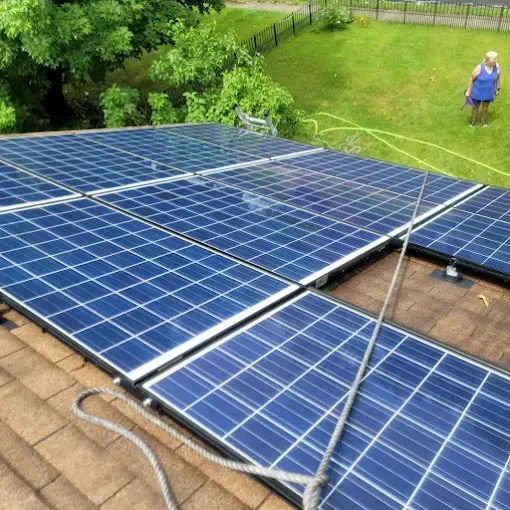 Solar panels on a brown roof, with a person watering grass in the background.