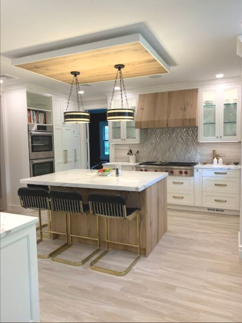 Kitchen ceiling detail with wood inset, over kitchen island with pendant lights, white cabinetry, and glass cabinet doors, wood reange hood