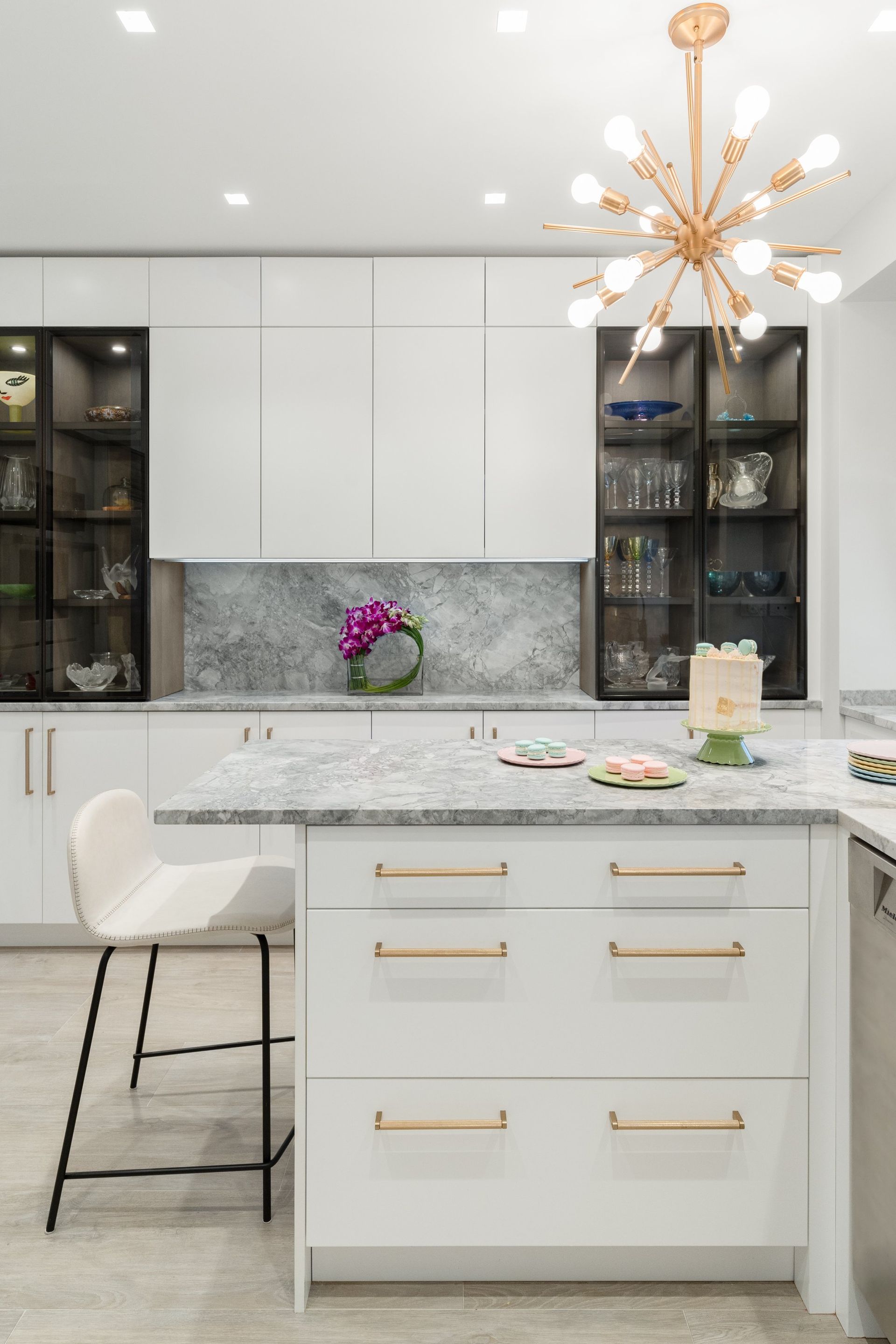White modern kitchen cabinets with gold starburst chandelier and glass display shelves