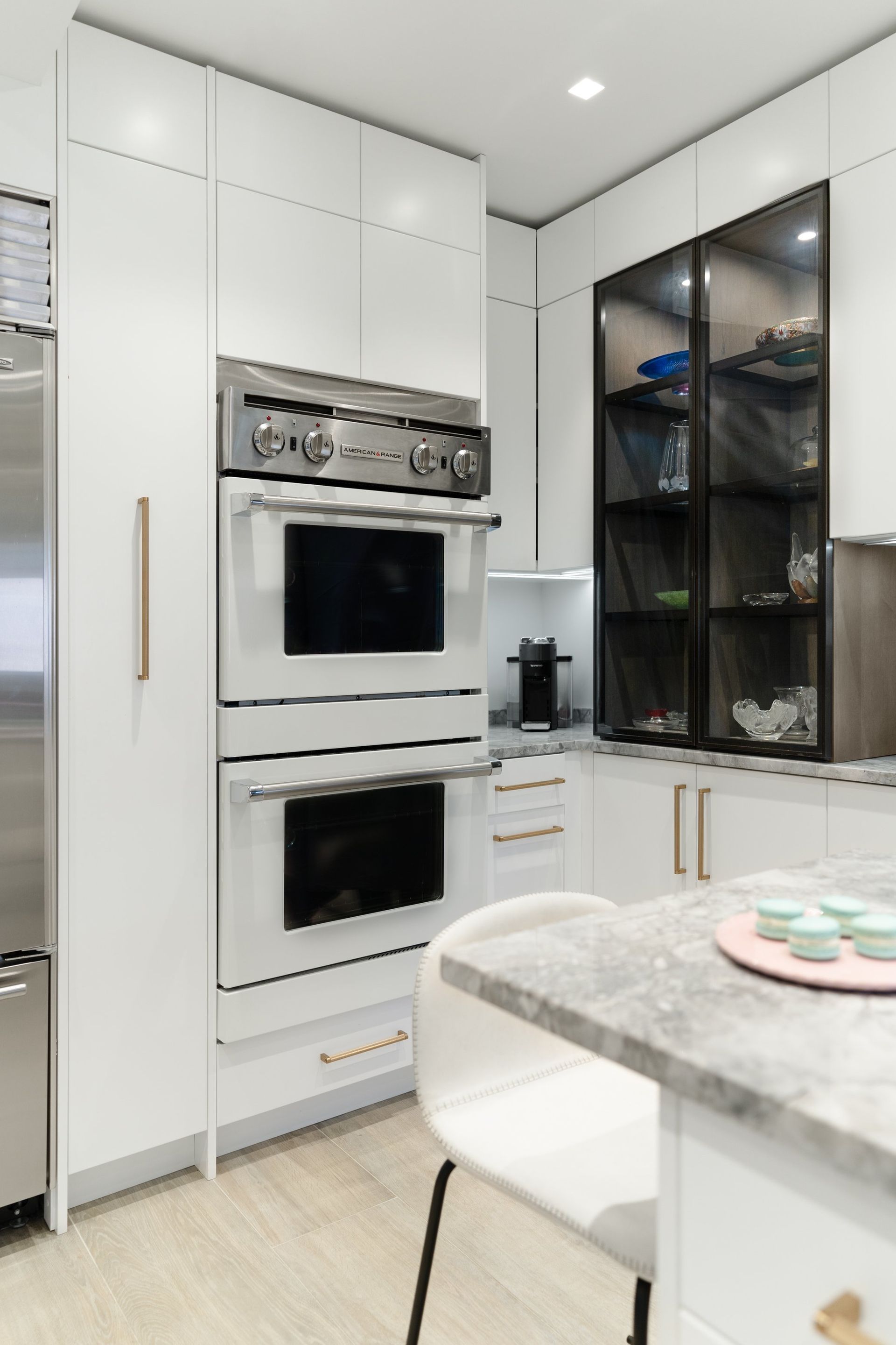 Modern white kitchen with built-in oven, tall cabinets, and black glass-front storage
