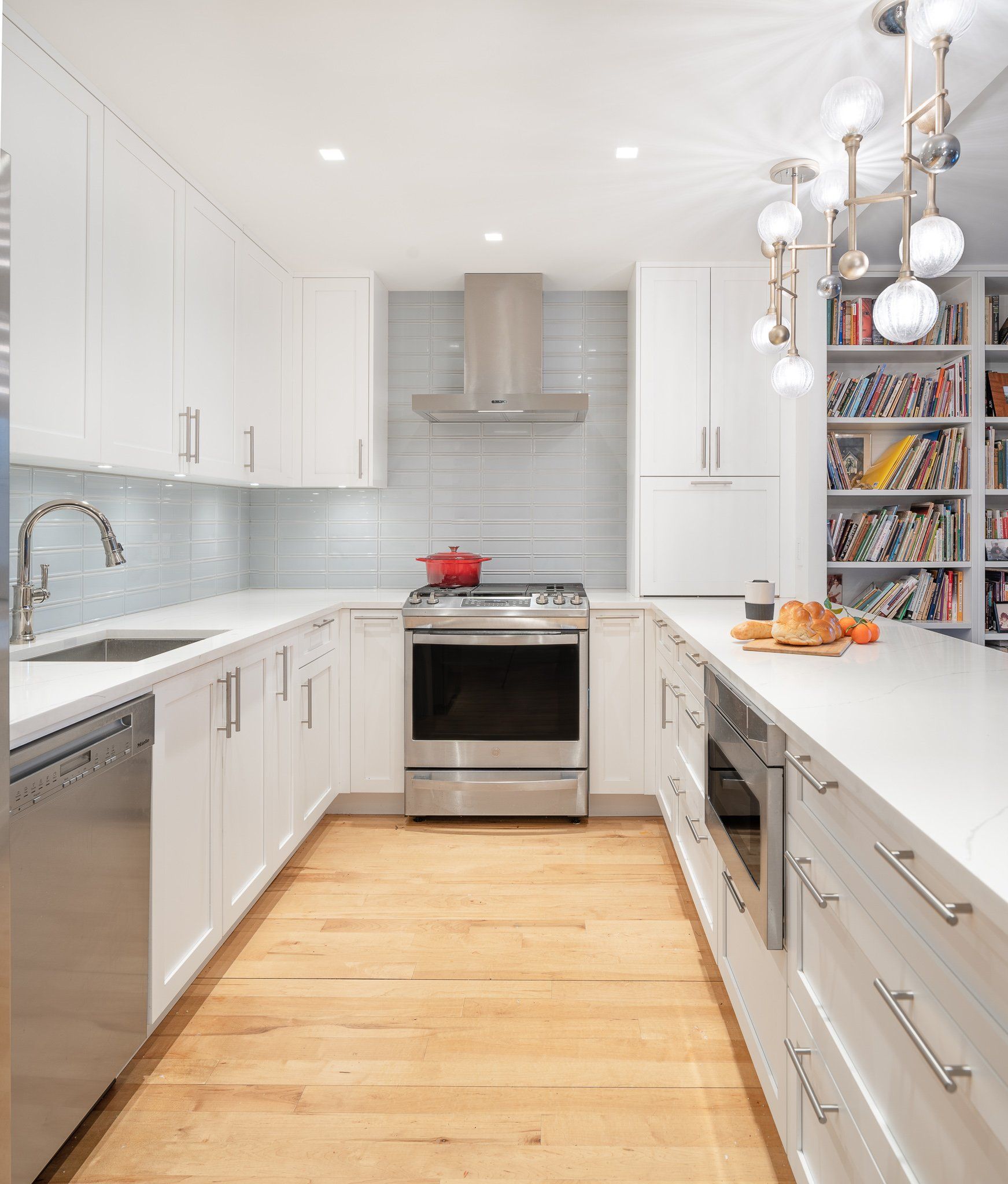 White kitchen with range hood, pendant lighting, built-in shelving, and bright modern finishes